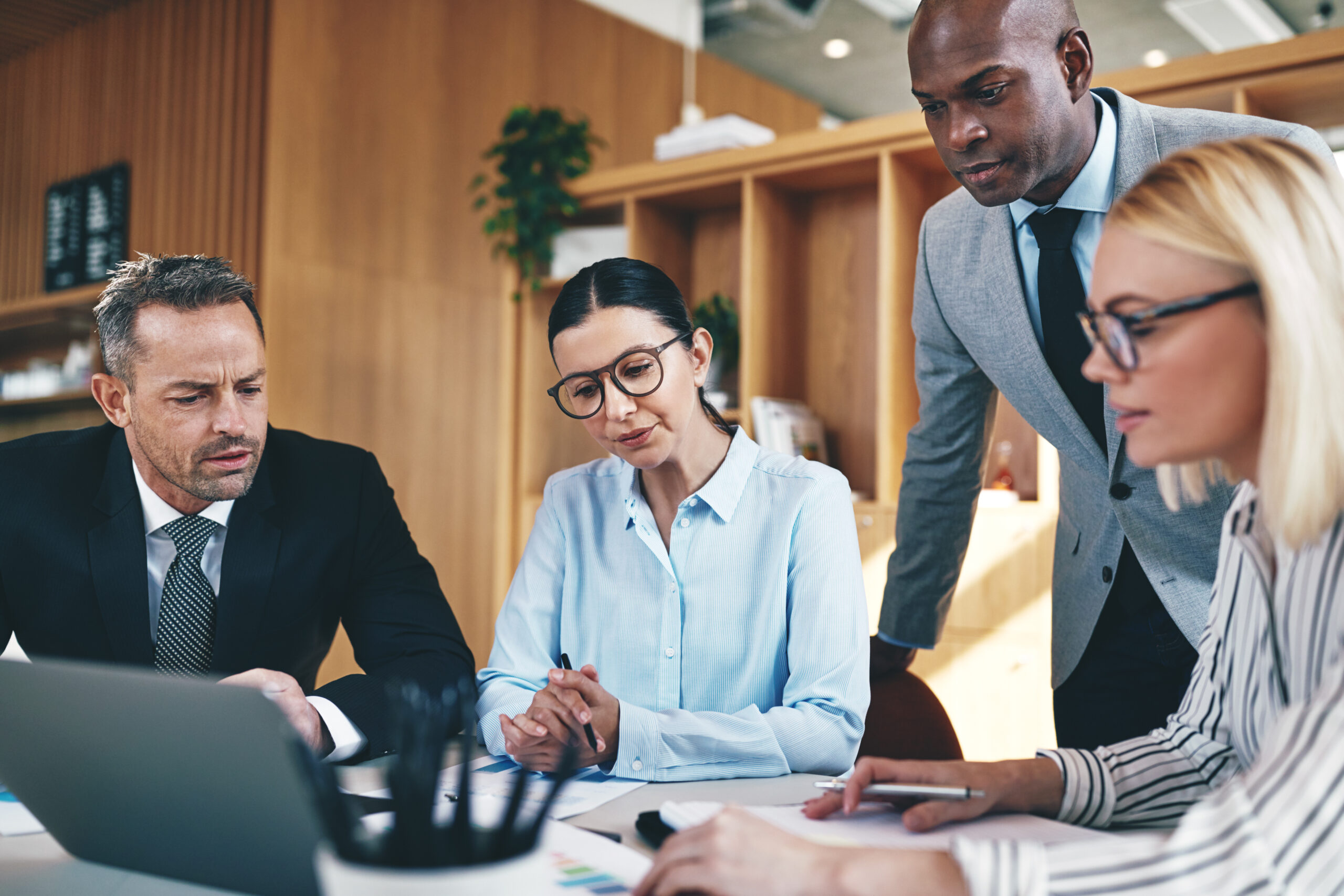 Diverse businesspeople going over paperwork together during an office meeeting Three business professionals in a meeting room, focused on a laptop during a collaborative discussion.