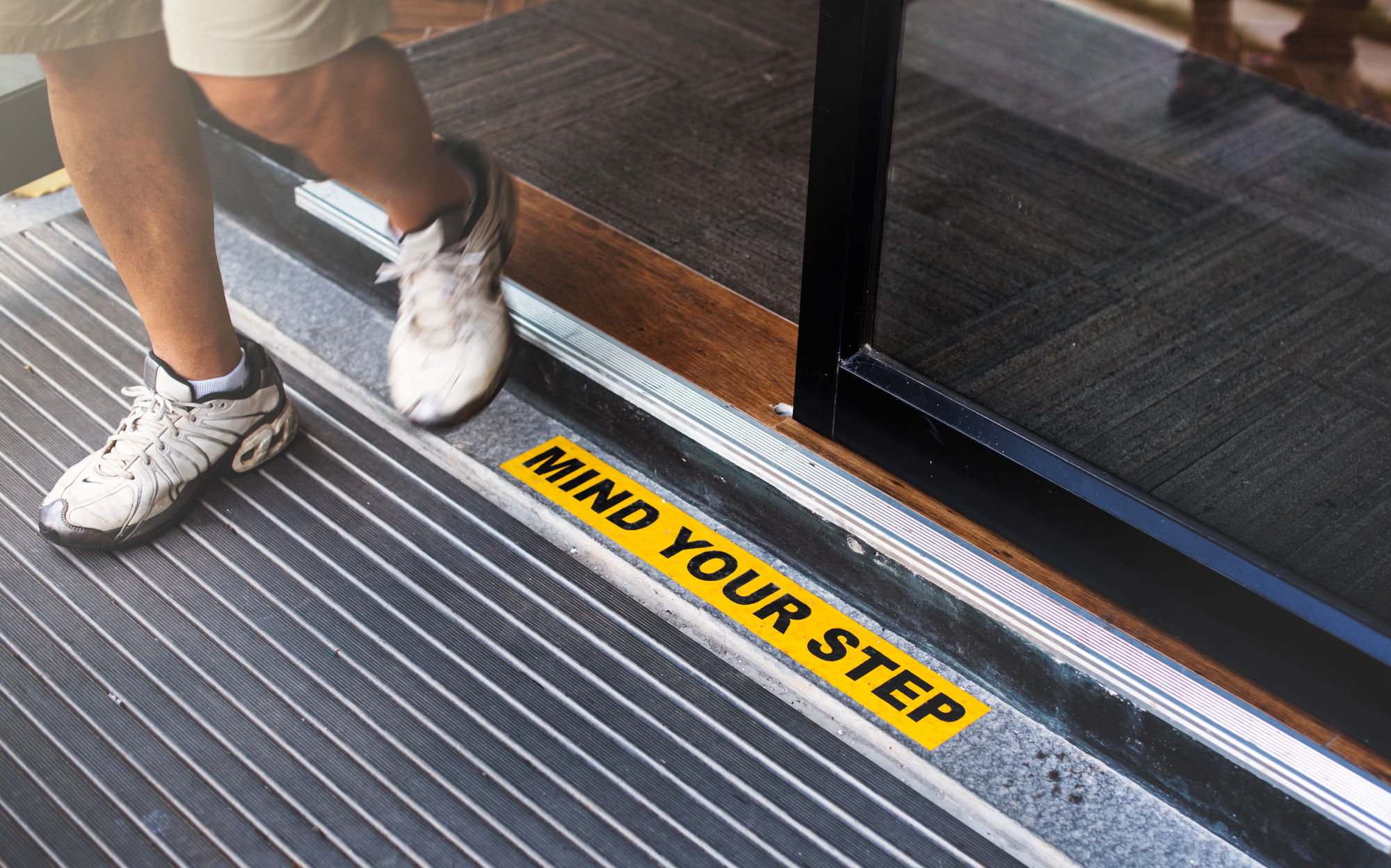 A person steps over a door threshold in a Sydney cafe, with a yellow sign on the floor that reads “MIND YOUR STEP.” The sign helps prevent accidents and potential injury compensation claims. A person steps over a door threshold in a Sydney cafe, with a yellow sign on the floor that reads "MIND YOUR STEP." The sign helps prevent accidents and potential injury compensation claims.