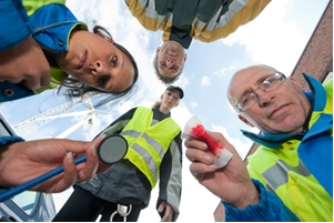 Four emergency responders in reflective vests and jackets look down toward the camera, one holding a stethoscope and another a bloody bandage, suggesting a medical emergency scene—a situation where public liability lawyers may be needed. The sky is visible in the background. Four emergency responders in reflective vests and jackets look down toward the camera, one holding a stethoscope and another a bloody bandage, suggesting a medical emergency scene—a situation where public liability lawyers may be needed. The sky is visible in the background.