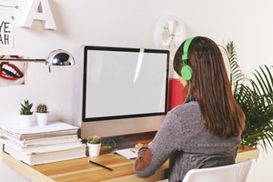 A person with long hair wearing green headphones sits at a desk, working on a computer with a blank screen—perhaps researching Total and Permanent Disability. The desk has stacked papers, cacti, and a lamp, with plants and wall decor in the background. A person with long hair wearing green headphones sits at a desk, working on a computer with a blank screen—perhaps researching Total and Permanent Disability. The desk has stacked papers, cacti, and a lamp, with plants and wall decor in the background.