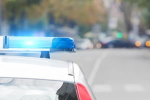 Close-up of a police car with blue lights flashing, parked on a blurred city street with trees and cars in the background, highlighting ongoing conversations about police brutality. Close-up of a police car with blue lights flashing, parked on a blurred city street with trees and cars in the background, highlighting ongoing conversations about police brutality.