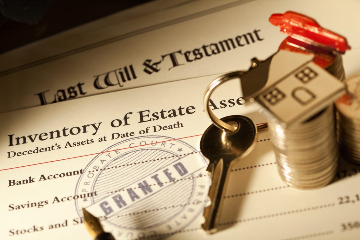 Close-up of a “Last Will & Testament,” an “Inventory of Estate” document, a key, a house-shaped keychain, stacks of coins, and a “Probate Court Granted” stamp in focus. Close-up of a “Last Will & Testament,” an “Inventory of Estate” document, a key, a house-shaped keychain, stacks of coins, and a “Probate Court Granted” stamp in focus.