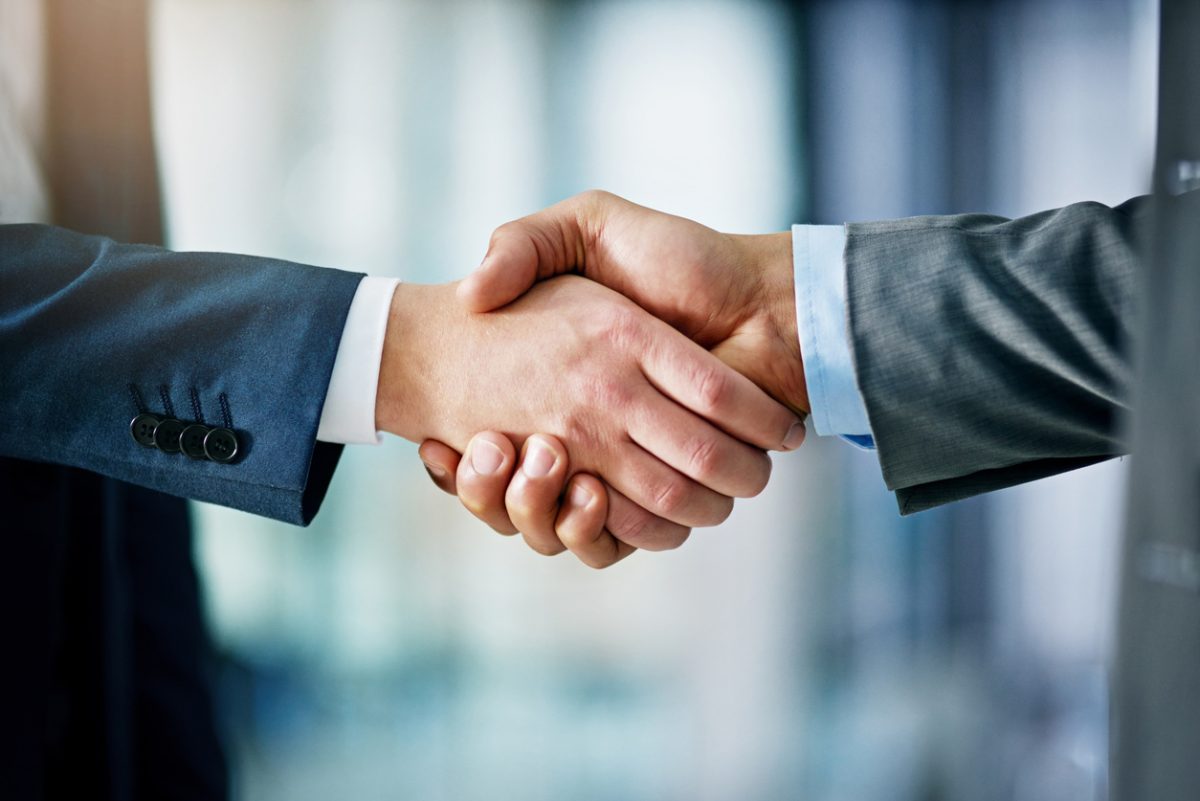 Two people in business suits shaking hands, symbolizing agreement or partnership, with a blurred office background. Two people in business suits shaking hands, symbolizing agreement or partnership, with a blurred office background.
