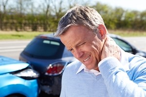 A man stands in front of two cars involved in a rear-end collision, holding his neck in pain, suggesting he may have whiplash or another injury from the accident. A man stands in front of two cars involved in a rear-end collision, holding his neck in pain, suggesting he may have whiplash or another injury from the accident.