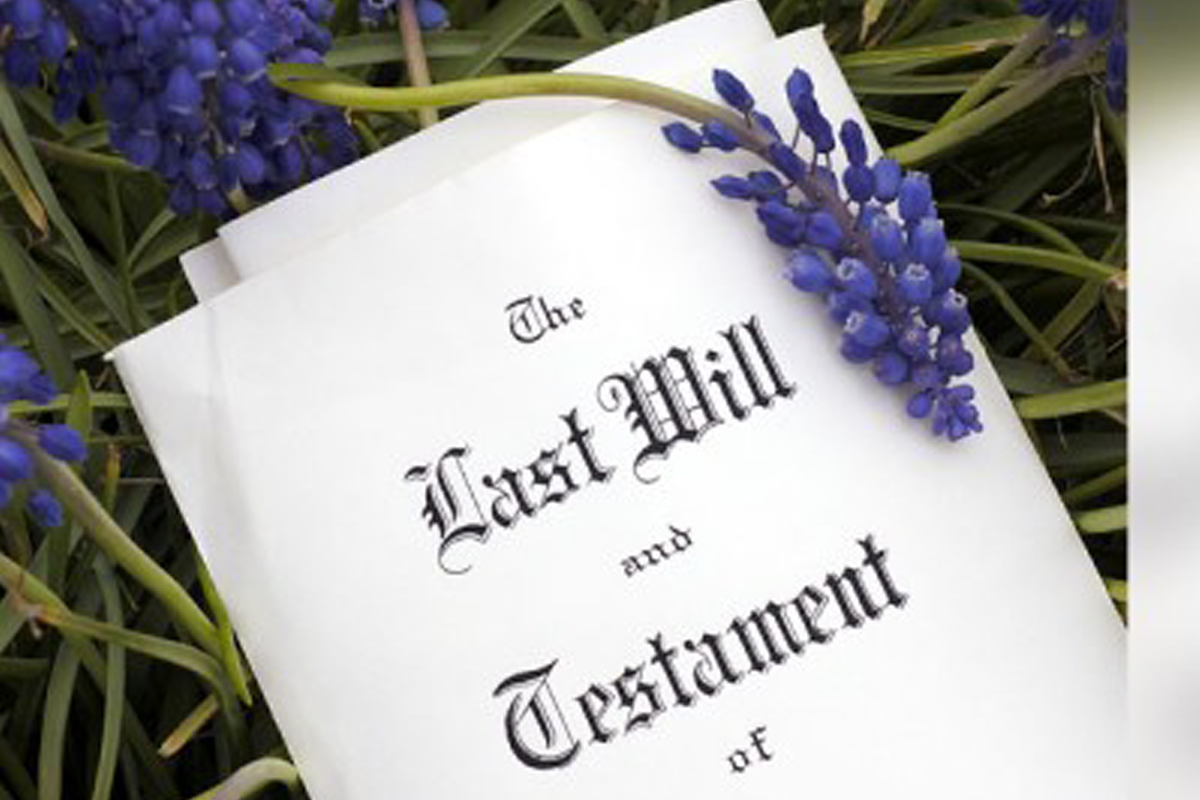A document titled “Last Will and Testament” lies on green grass with purple grape hyacinth flowers resting on top. A document titled “Last Will and Testament” lies on green grass with purple grape hyacinth flowers resting on top.