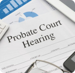 A document titled “Probate Court Hearing” on a desk, surrounded by a pair of glasses, a chart, a calculator, and part of a tablet. A document titled "Probate Court Hearing" on a desk, surrounded by a pair of glasses, a chart, a calculator, and part of a tablet.