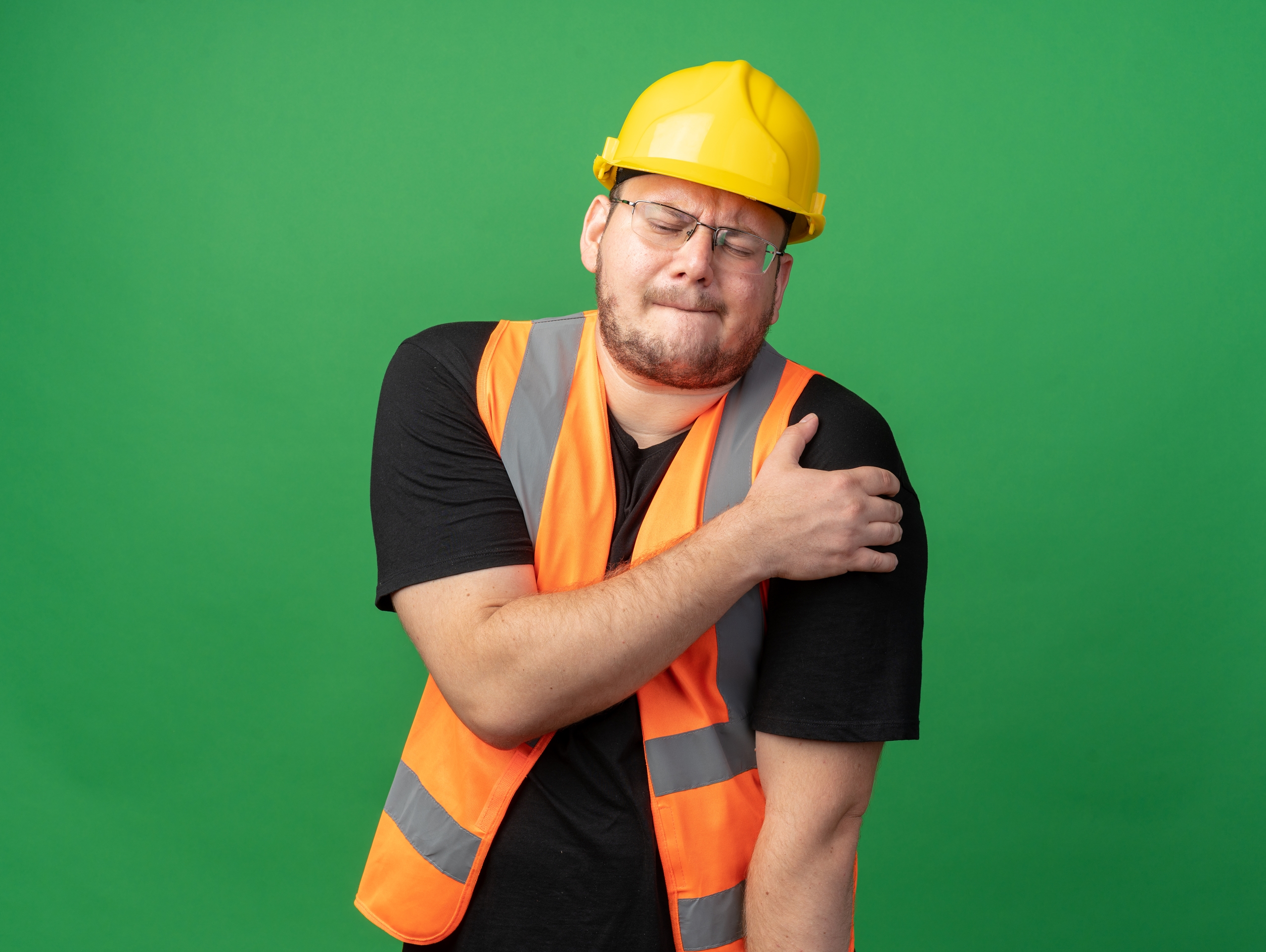 builder man in construction vest and safety helmet looking unwell touching his shoulder feeling pain standing over green background builder man in construction vest and safety helmet looking unwell touching his shoulder feeling pain standing over green background